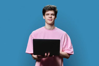Laptop kullanan genç bir üniversite öğrencisi, mavi stüdyo geçmişi var. Kameraya bakan kendine güvenen bir adam. İnternet teknolojileri, çevrimiçi öğrenim istirahatı, sanal uzaktan eğitim eğlence iletişimi