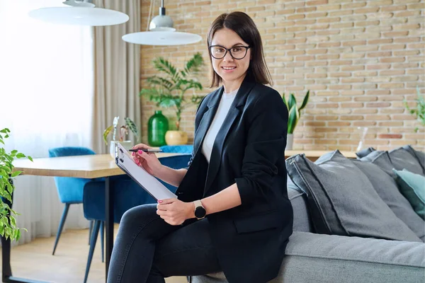 Portrait of young female psychologist with clipboard in modern office. Confident friendly woman professional mental therapist. Therapy service, psychology, psychotherapy, advice, support, treatment