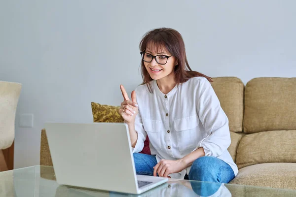 リビングルームでソファーに座っている成熟した女性は ビデオオンライン会議のチャットコールを持っているラップトップスクリーンを見て 話します ビジネスレジャー ブログ コミュニケーション テクノロジー — ストック写真