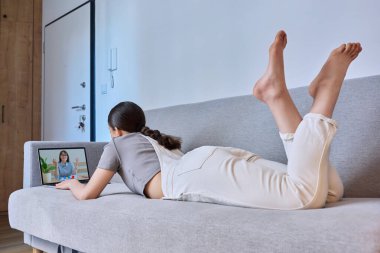 Evdeki kanepede oturan psikologla çevrimiçi terapi seansında genç bir bayan. Terapist danışmanıyla sanal görüşmede dizüstü bilgisayar kullanan genç bir kız. Psikoloji, akıl sağlığı, ergenlik kavramı.