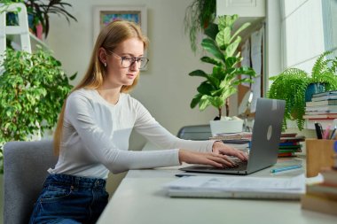 Evde dizüstü bilgisayarda yazan gülümseyen genç kız. Kadın serbest çalışan, uzaktan çalışan bir çalışan, internetten sınavlara hazırlanan bir üniversite öğrencisi. Teknoloji gençlik eğitimi çalışmaları