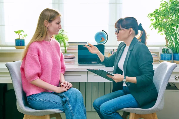 Young female at therapy meeting with psychotherapist. Session of teenage student girl, psychologist with clipboard talking to patient. Psychology, psychotherapy, treatment, youth mental health
