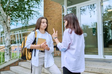 Sırt çantalı liseli kız öğrenci kadın öğretmenle, akıl hocasıyla, koçla konuşuyor, eğitim binasının merdivenlerinde dikiliyor. Ergenlik, eğitim, bilgi, iletişim