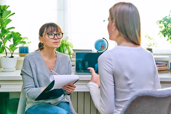 Young female at therapy meeting with psychotherapist. Session of teenage student girl, psychologist with clipboard talking to patient. Psychology, psychotherapy, treatment, youth mental health