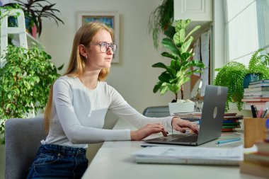 Evde dizüstü bilgisayarda yazan gülümseyen genç kız. Kadın serbest çalışan, uzaktan çalışan bir çalışan, internetten sınavlara hazırlanan bir üniversite öğrencisi. Teknoloji gençlik eğitimi çalışmaları
