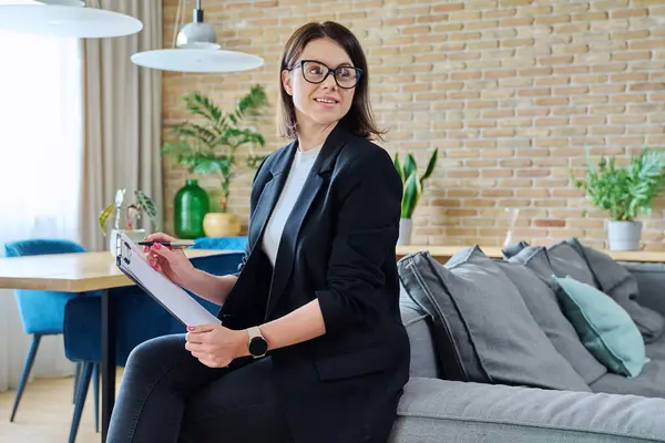 Portrait of young female psychologist with clipboard in modern office. Confident friendly woman professional mental therapist. Therapy service, psychology, psychotherapy, advice, support, treatment