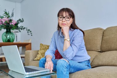 Oturma odasında dizüstü bilgisayarı olan orta yaşlı bir kadının portresi. Kendine güveni tam, başarılı bir kadın. 45 yaşında.