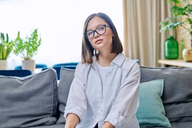 Kendinden emin gülümseyen, gözlüklü, beyaz gömlekli, oturma odasında kameraya bakan başarılı genç bir kadının portresi. Güzellik, güven, başarı, yaşam tarzı, insan kavramı