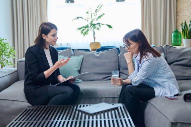 Terapi toplantısında orta yaşlı üzgün bir kadın modern klinikteki koltukta oturup psikolog psikoterapistle konuşuyor. Olgun hastalar, akıl sağlığı, destek hizmetleri