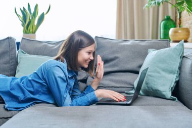 Genç bir kadın evdeki kanepede dizüstü bilgisayarla görüntülü sohbet konferansı yapıyor. Video blogu kaydeden kadın, arkadaşlarıyla çevrimiçi yayın yapıyor iş hayatı hakkında konuşuyor.