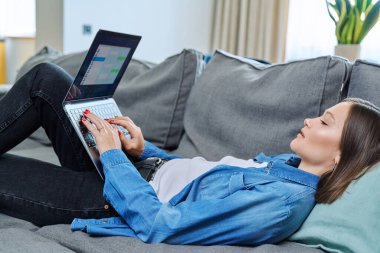 Oturma odasındaki kanepede uzanmış genç bir kadın bilgisayarı internet iletişimi için kullanıyor arkadaşlarıyla, iş arkadaşlarıyla, ailesiyle sohbet ediyor. İnsanlar, teknoloji, yaşam tarzı konsepti
