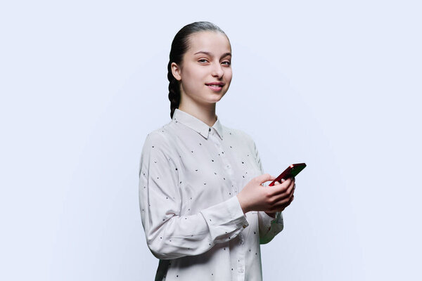 Teenage student, girl 15, 16 years old with smartphone looking at camera on white studio background. Adolescence, internet technologies, mobile online applications apps services for learning leisure