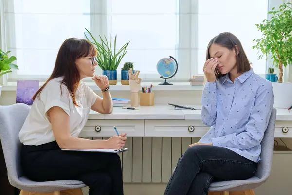Sad stressed young woman in therapy with professional psychologist. Women talking in office, therapist counselor psychotherapist working with patient. Support, mental health, psychology, psychotherapy