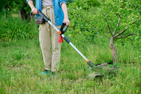 Woman mowing grass using manual electric lawn mower cordless garden grass trimmer. Spring summer seasonal work in the garden