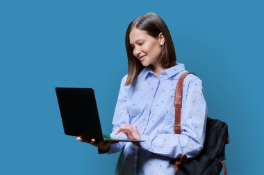 Mavi stüdyo geçmişinde dizüstü bilgisayarı olan genç bir kadın. Gülümseyen kız öğrenci bilgisayar kullanıyor, ekranda poz veriyor. Eğitim, iş, iş, eğlence, gençlik teknolojileri