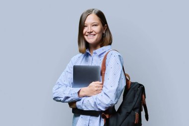 Gri stüdyo arka planında dizüstü bilgisayarı olan genç bir kadın. Gülümseyen kız öğrenci kameraya bakıyor. Eğitim, iş, iş, eğlence, gençlik kavramı teknolojileri