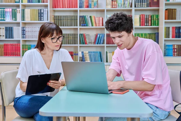 Mature female college counselor, social worker talking with student young male, meeting in library office. Youth mental health, psychology, psychotherapy, help, consultation, mentorship concept