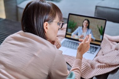 Çevrimiçi zihinsel terapi, orta yaşlı bir kadının evde psikolog terapist sosyal hizmet görevlisiyle dizüstü bilgisayar kullanarak koltukta yatması. Psikoloji psikoterapi destek tedavisi