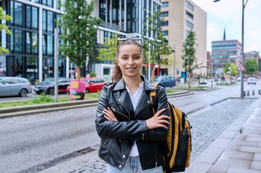 Genç lise öğrencisinin portresi. 16-17 yaşlarında, sırt çantalı, modern şehrin sokaklarında kameraya bakan kendine güvenen bir kız. Şehir hayatı, ergenlik, eğitim, gençlik kavramı