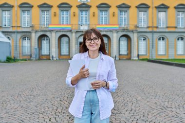 Orta yaşlı kadın öğretmen, akıl hocası ve pedagogun açık hava portresi bir eğitim binasının, üniversite üniversitesinin arka planında poz veriyor.