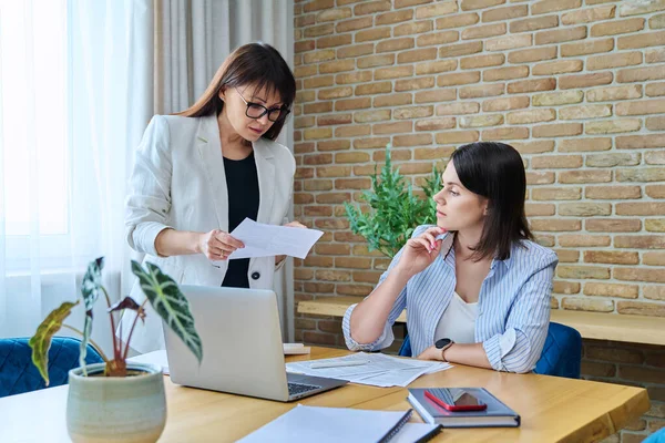 Two serious business women colleagues sitting at large table in office with business papers contracts. Business ceo work law finance mentoring consulting teamwork people job concept