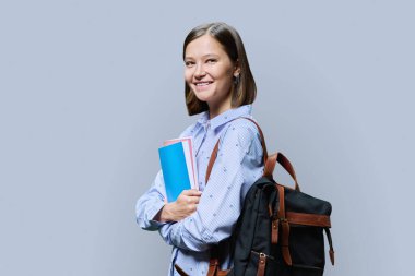 Gri stüdyo arka planında sırt çantası dolusu ders kitabı olan genç üniversite öğrencisinin portresi. Kameraya bakan kendinden emin 20 'li yaşlarda bir kadın. Eğitim, bilgi, yaşam tarzı, gençlik kavramı