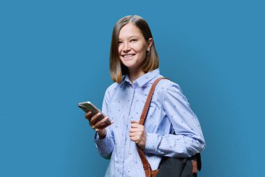 Mavi stüdyo geçmişinde akıllı telefon çantalı genç bir kız öğrenci. Kameraya bakıp gülümseyen çekici kadın. İş dünyası için mobil uygulamalar, eğlence, teknoloji ve insan kullanımı.