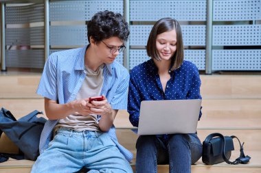 Arkadaşları üniversite öğrencisi erkek ve kız eğitim binasının içinde akıllı telefon dizüstü bilgisayarı var. Gençlik, yaşam tarzı, teknoloji, eğlence iletişimi için mobil uygulamalar