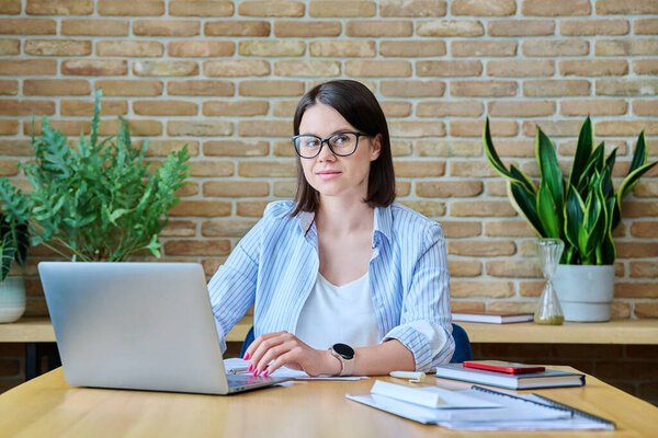 Portrait of young business woman sitting at workplace in office, smiling female looking at camera. Business management, finance, law, logistics, sales, services concept