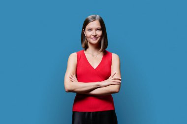 Mavi stüdyo arka planında kendine güvenen genç bir kadının portresi. Kollarını kavuşturup kameraya bakan başarılı, modaya uygun bir kadın. İş, iş, hizmet, eğitim, moda güzellik meslekleri