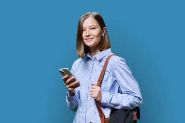 Mavi stüdyo geçmişinde akıllı telefon çantalı genç bir kız öğrenci. Kameraya bakıp gülümseyen çekici kadın. İş dünyası için mobil uygulamalar, eğlence, teknoloji ve insan kullanımı.