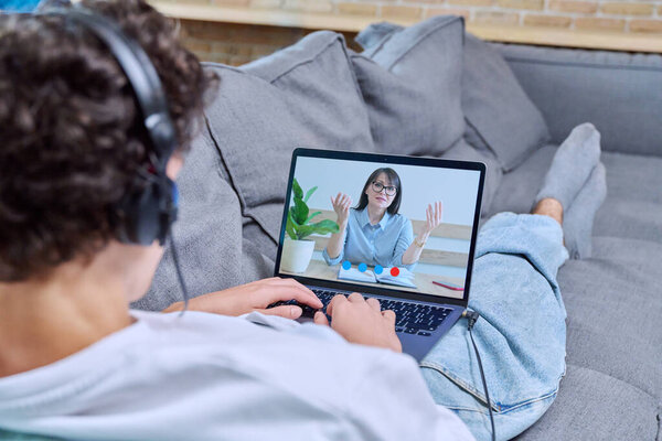 Online meeting with psychologist, young man lying on couch at home talking to female therapist using video conference call on laptop. Psychology, psychotherapy, treatment, mental health concept