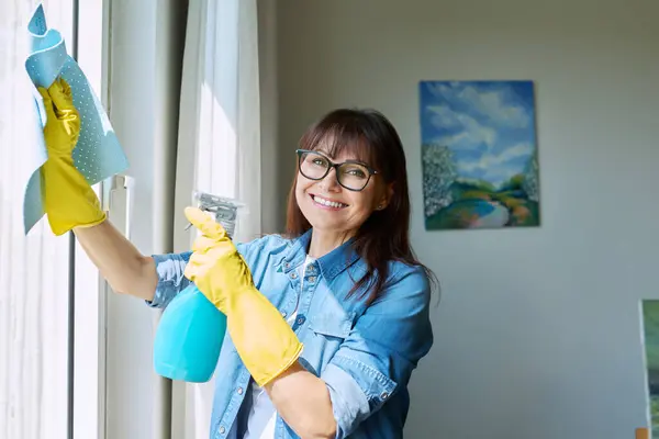 Medelålders Kvinna Handskar Med Sprayrengöringsfönster Hemma Leende Kvinna Tittar Kameran — Stockfoto