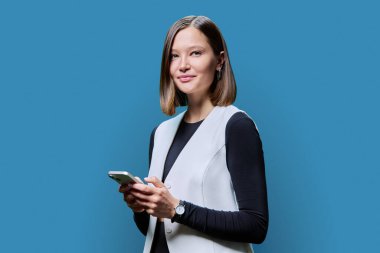 Genç trend iş kadını mavi arka planda akıllı telefon kullanıyor. Gülümseyen şık bayan mesajlaşması. Teknoloji mobil uygulamaları İnternet işi iletişim eğitimi