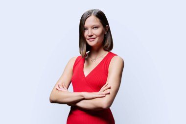 Beyaz stüdyo arka planında kırmızı elbiseli, kendine güvenen genç bir kadının portresi. Kollarını kavuşturup kameraya bakan başarılı, modaya uygun bir kadın. İş, iş, hizmet, eğitim, moda güzellik meslekleri