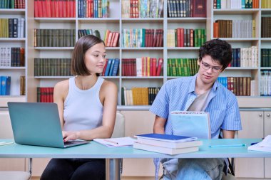 Genç erkek ve bayan öğrenciler üniversite kütüphanesinde masalarında oturuyorlar, ellerinde kitaplar, defterler, çalışmalar, sınavlara hazırlanmalar. Bilgi, eğitim, gençlik, üniversite konsepti
