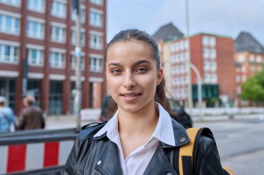 Genç lise öğrencisinin portresi. 16-17 yaşlarında, sırt çantalı, modern şehrin sokaklarında kameraya bakan kendine güvenen bir kız. Şehir hayatı, ergenlik, eğitim, gençlik kavramı