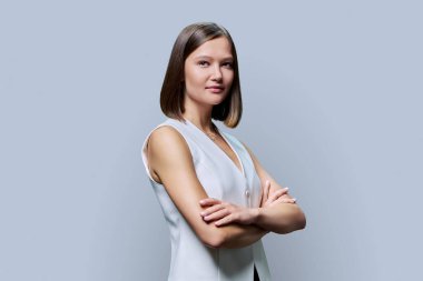 Gri stüdyo arka planında kameraya bakan kollarını çapraz bağlamış, kendine güvenen, ciddi bir kadın. Güzellik, iş, iş... Girişimcilik... İşletme uzmanlığı...