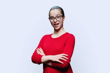 Portre, beyaz arka planda kırmızı gözlüklü neşeli genç kızı şaşırttı. Pozitif kadın, 16-17 yaşlarında çapraz kollu lise öğrencisi bir gençle kameraya bakıyor.