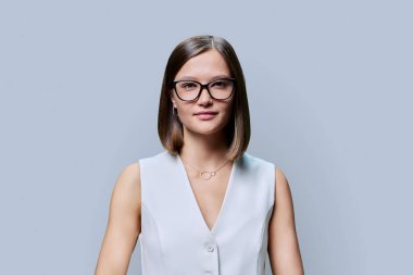 Gözlüklü güzel bir kadının portresi, gri stüdyo arka planında doğal makyaj stili olan kadın yüzü. Güzellik bakımı saç, iş eğitimi moda, sağlık vizyonu gözler