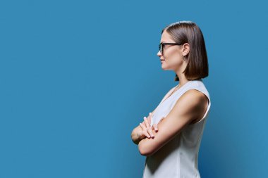 Profil görüntüsü, çapraz kollu gözlük takan başarılı genç iş kadını, fotokopi mavi stüdyo arka planı, reklam metni için alan. İş hizmetleri eğitimcileri