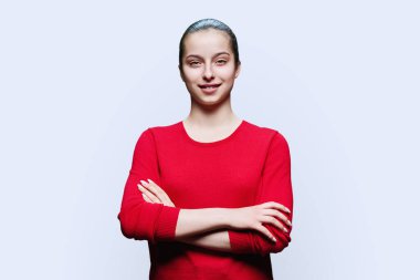 Beyaz arka planda kendine güvenen kırmızı elbiseli genç kız portresi. Pozitif kadın, 16-17 yaşlarında çapraz kollu lise öğrencisi bir gençle kameraya bakıyor.