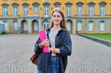 Açık havada poz veren genç kız öğrencinin portresi, eğitim binasının arka planı. Çantayla gülümseyen kadın, kameraya bakan ders kitabı. Gençlik, eğitim, üniversite, üniversite