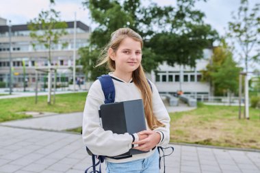 Sırt çantalı, dijital tabletli okul binası geçmişi olan gülümseyen kız öğrenci portresi. Okula, çocukluğa, eğitim bilgi öğrenme kavramına