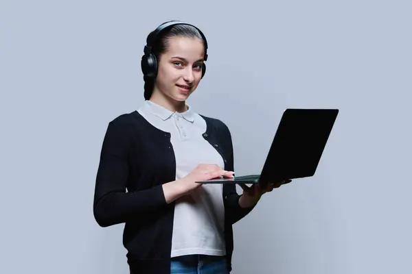 Nastoletnia Studentka Nosząca Słuchawki Pomocą Laptopa Patrząca Kamerę Szarym Tle — Zdjęcie stockowe