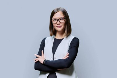 Genç, kendine güvenen, gözlüklü, çapraz kollu ciddi bir kadın gri stüdyo arka planındaki kameraya bakıyor. Güzellik, iş, iş... Girişimcilik... İşletme uzmanlığı...