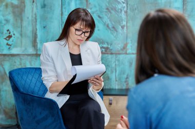 Orta yaşlı kadın psikolog. Elinde dosya var. Ofis sandalyesinde hastayla çalışıyor. Olgun kadın profesyonel psikoterapist psikoterapist sosyal hizmet görevlisi, işyeri