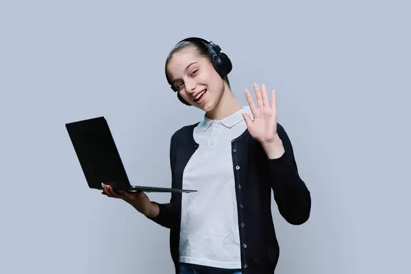 十几岁的女生戴着耳机 用笔记本电脑 在灰色的工作室背景上看着相机 视听互联网技术在教育学习 在线课程 青少年高中概念中的应用 — 图库照片