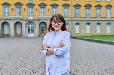 Kendine güvenen orta yaşlı kadın öğretmen, akıl hocası, kollarını kavuşturmuş poz veren pedagog. Eğitim binası, üniversite üniversitesi.