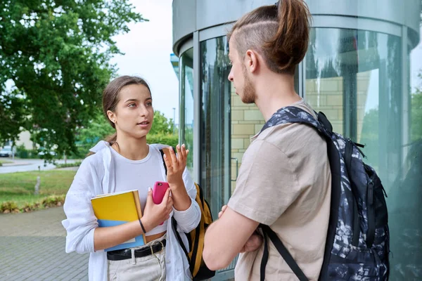 Meeting of two teenage students, guy and girl, outdoors near educational building. Friendship, communication, education, high school college concept